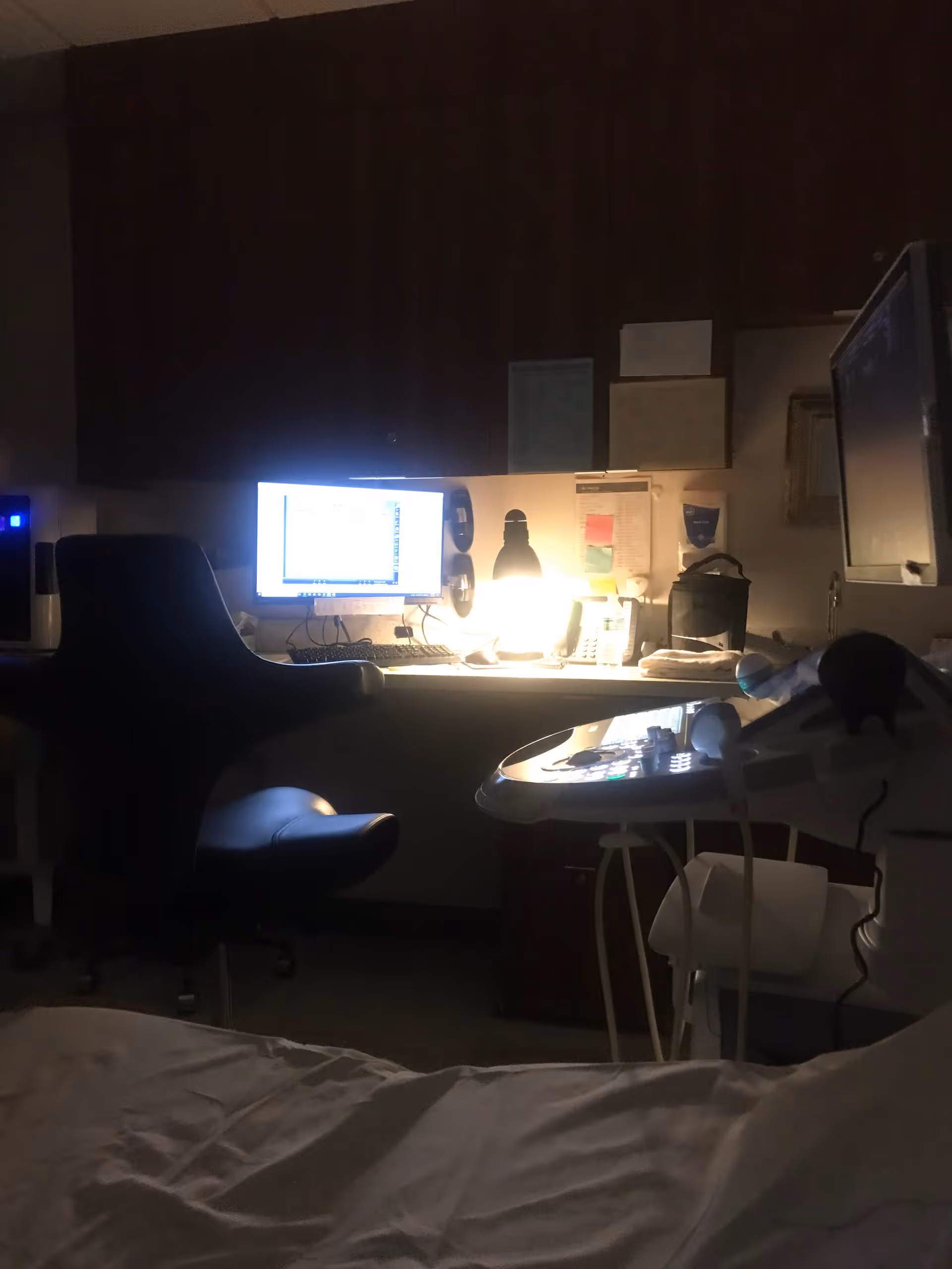 Dim interior of a nurse station with computer, monitor, phone, and medical equipment.