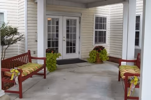 Covered front entrance with two red benches, potted plants, and double glass doors.