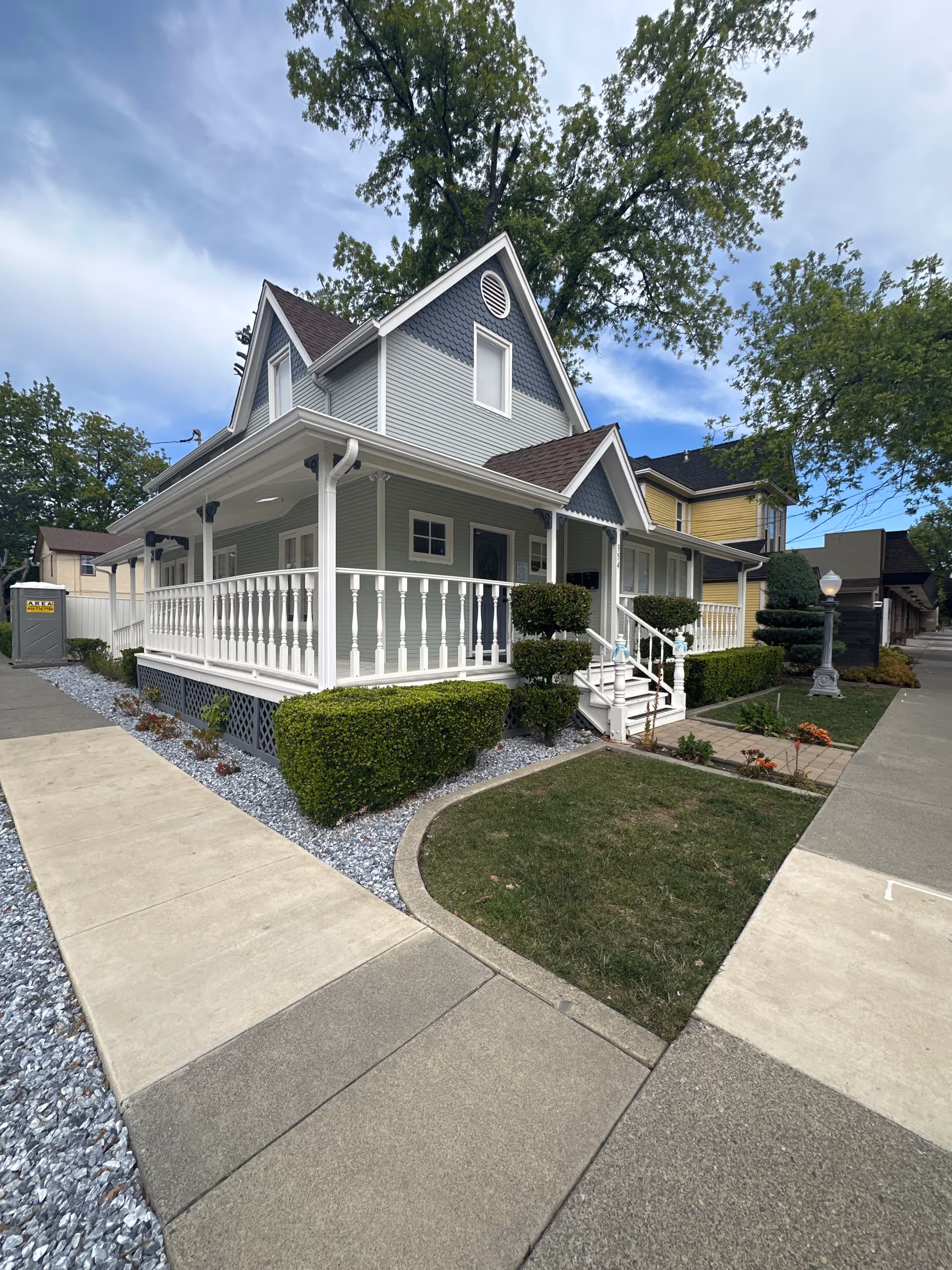 Exterior view of a gray two-story house with a wraparound porch and trimmed landscaping.