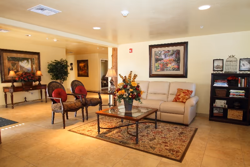 A cozy living room lounge with sofa, chairs, coffee table, rug, and framed art.