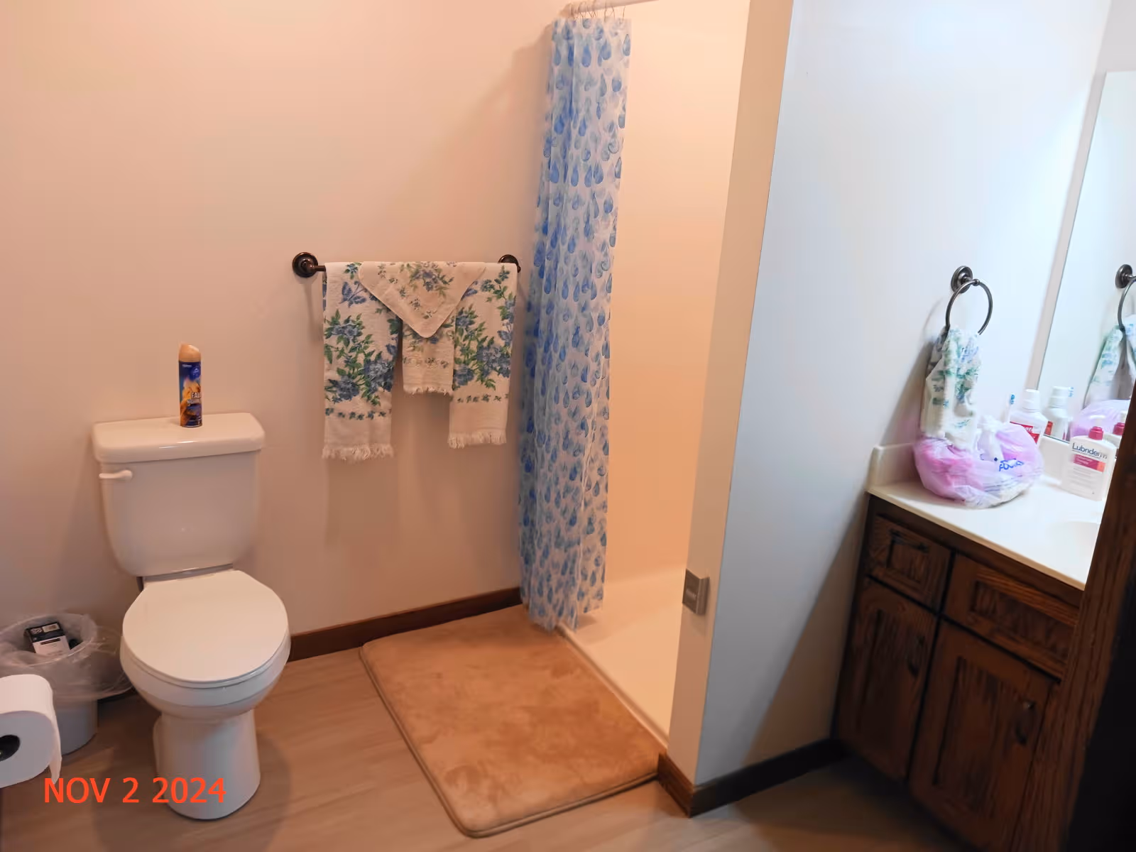 Bathroom with toilet, shower, blue curtain, towels, and wooden vanity.