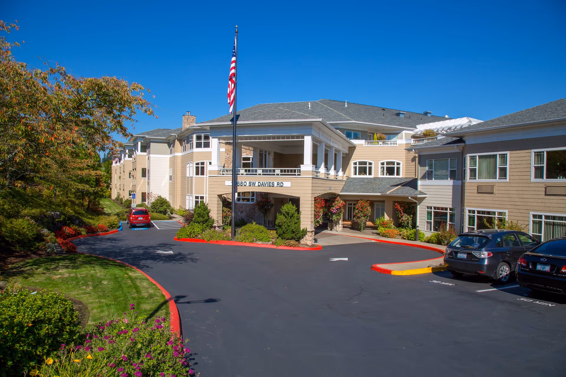 Exterior view of Hearthstone at Murrayhill showing entrance, flagpole, driveway, and parked cars.