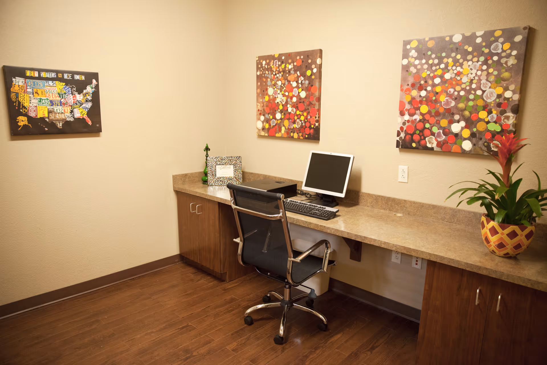 A workstation with computer, chair, and colorful art on beige walls in a quiet office.
