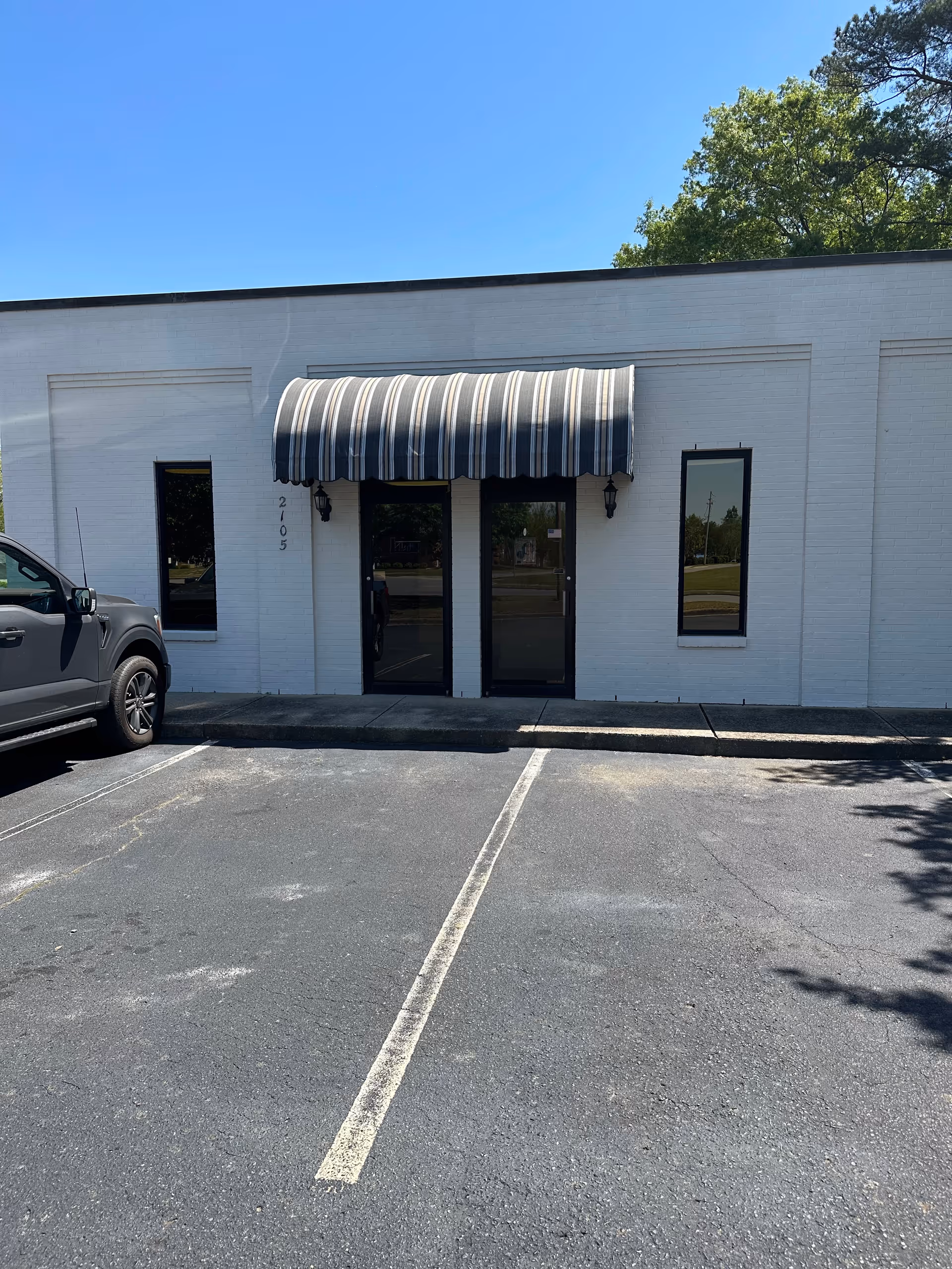 White storefront with striped awning over double doors and a parking lot in front.