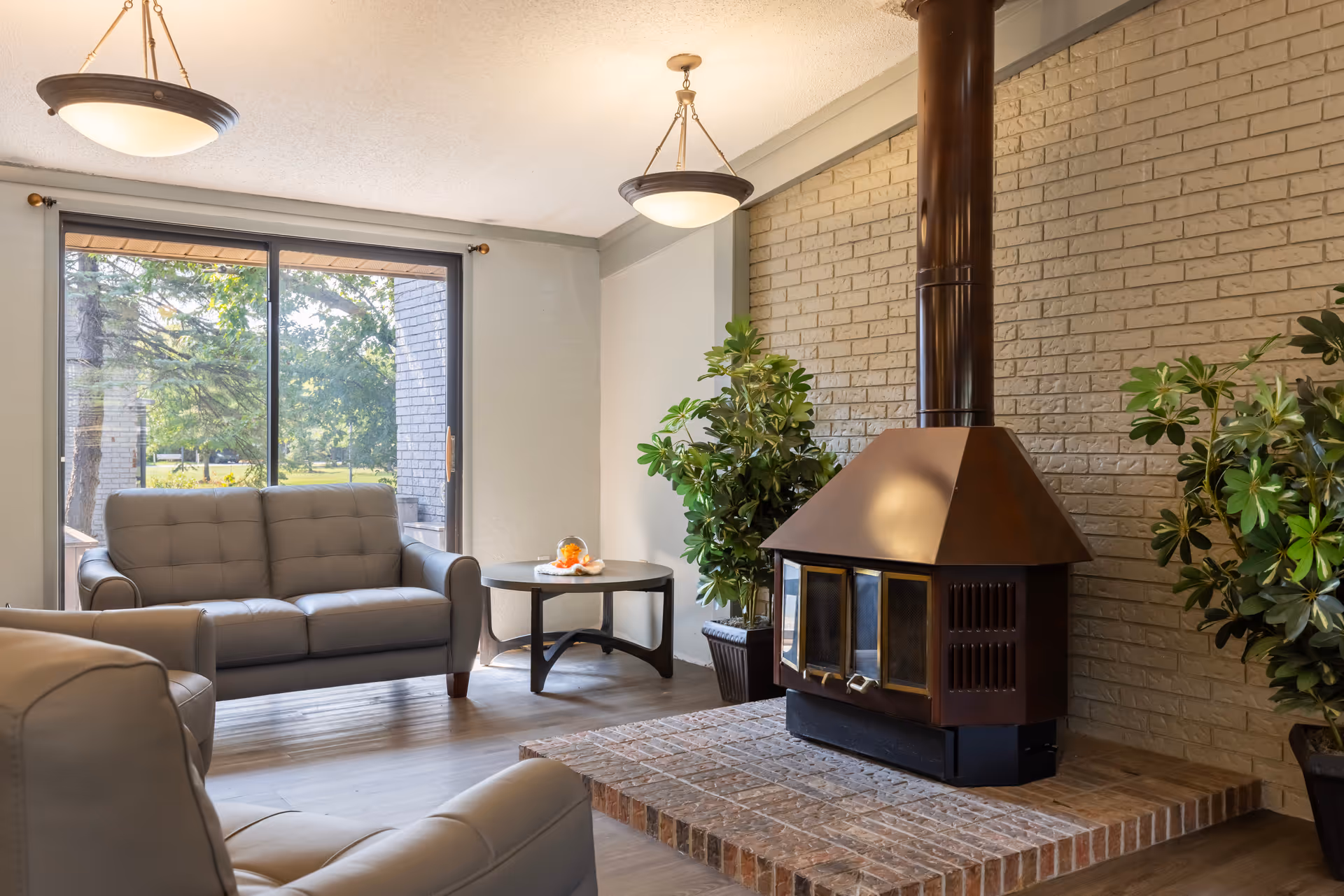 Cozy living room lounge with brick fireplace, seating, and a large window view.