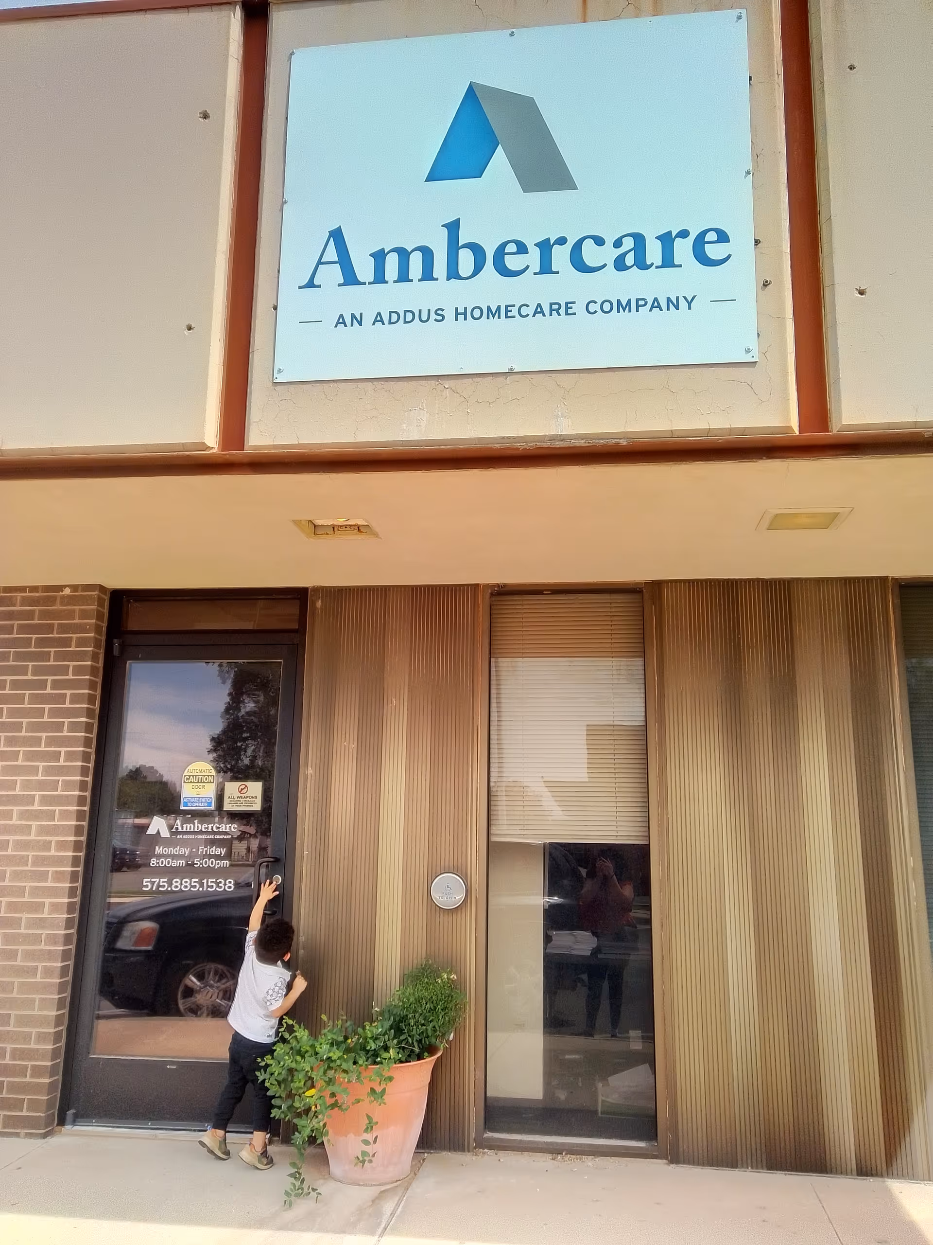 Exterior of Ambercare facility with entrance door, large sign, and a potted plant nearby.