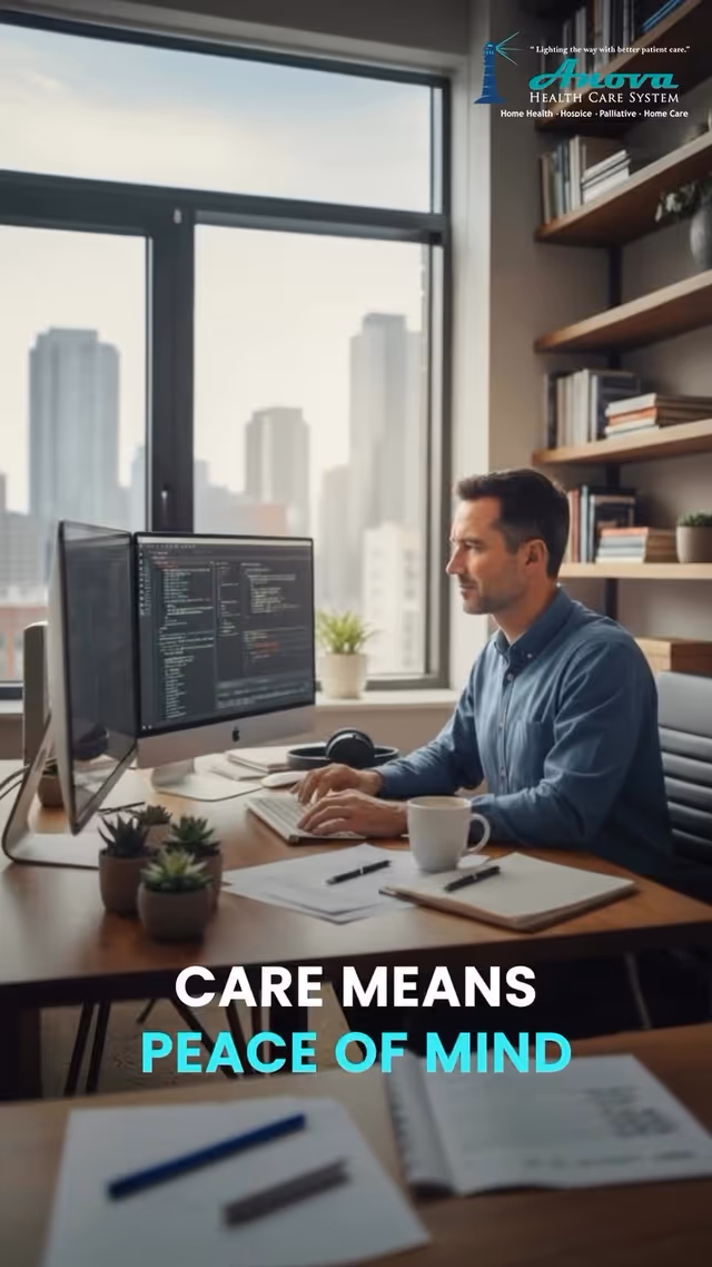 A man works at a desk with dual monitors by a large window in an office.