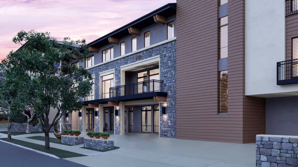 Modern multi-story senior living building with stone facade, balconies, and landscaped entrance.