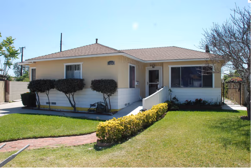 Single-story beige senior living building with a ramp and manicured front lawn.
