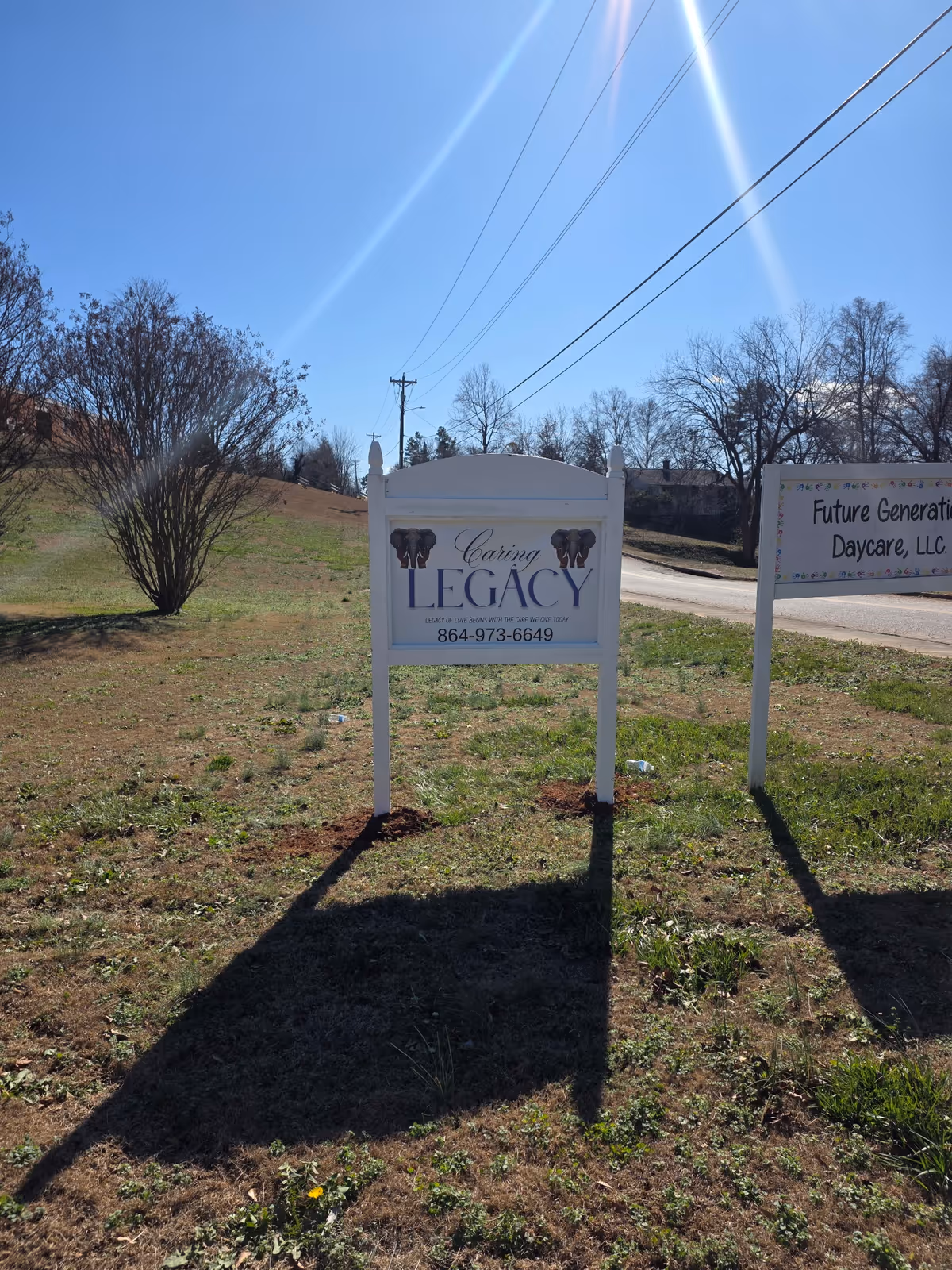 Outdoor lawn with Caring Legacy sign and another daycare sign beside a road.