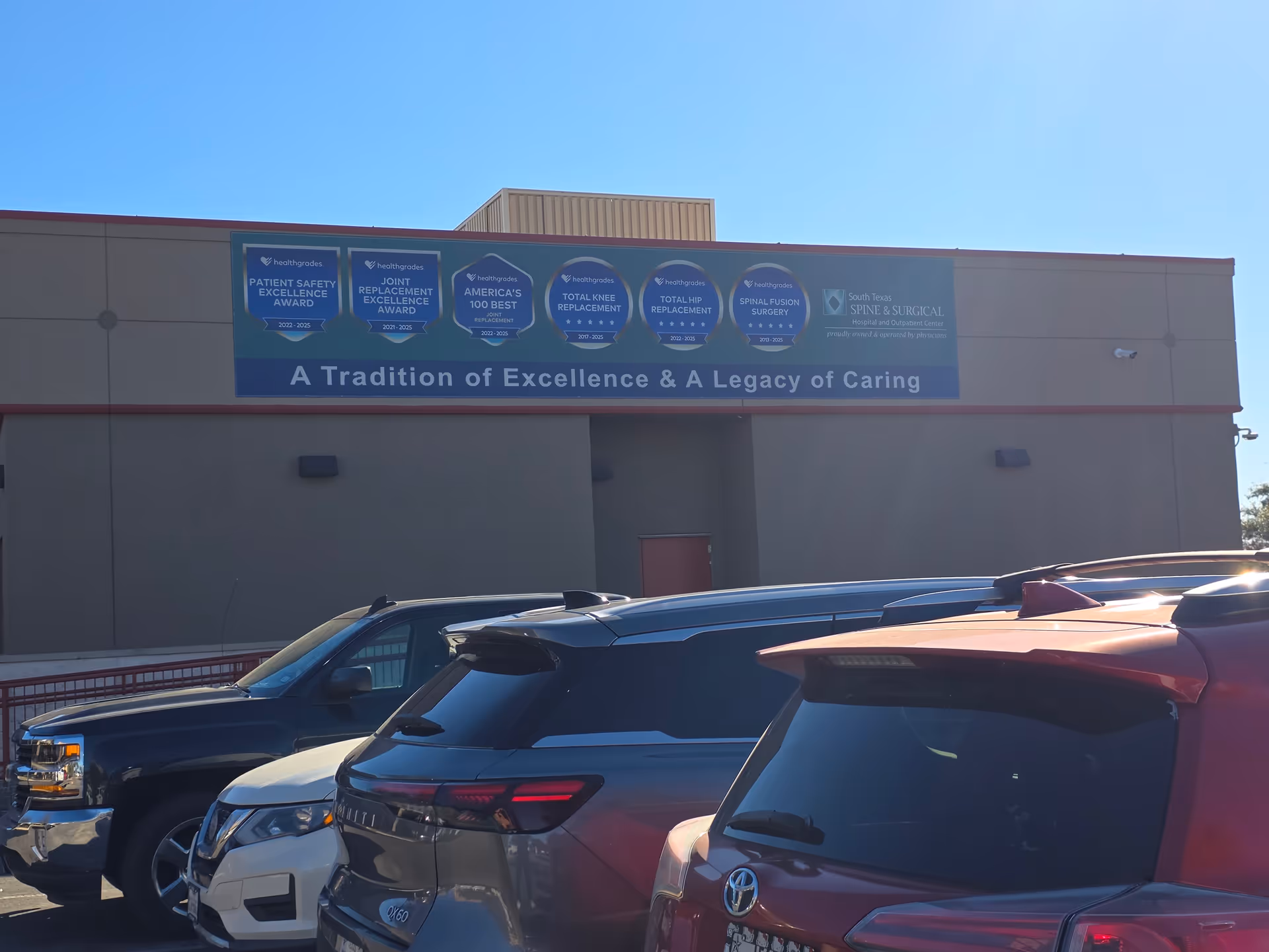 Exterior view of South Texas Spine and Surgical Hospital with a banner and parked cars.
