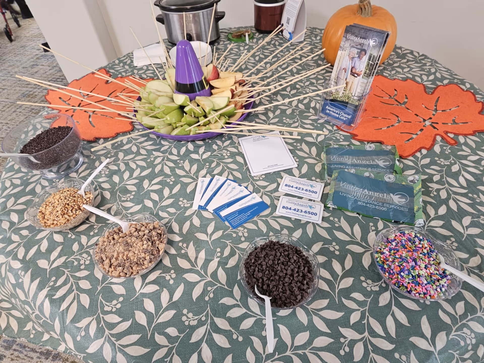 Indoor table with a fruit centerpiece, snack bowls, and Visiting Angels brochures.