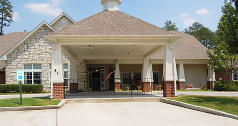 Front exterior of a senior living facility with a covered entrance, brick columns, and a driveway.