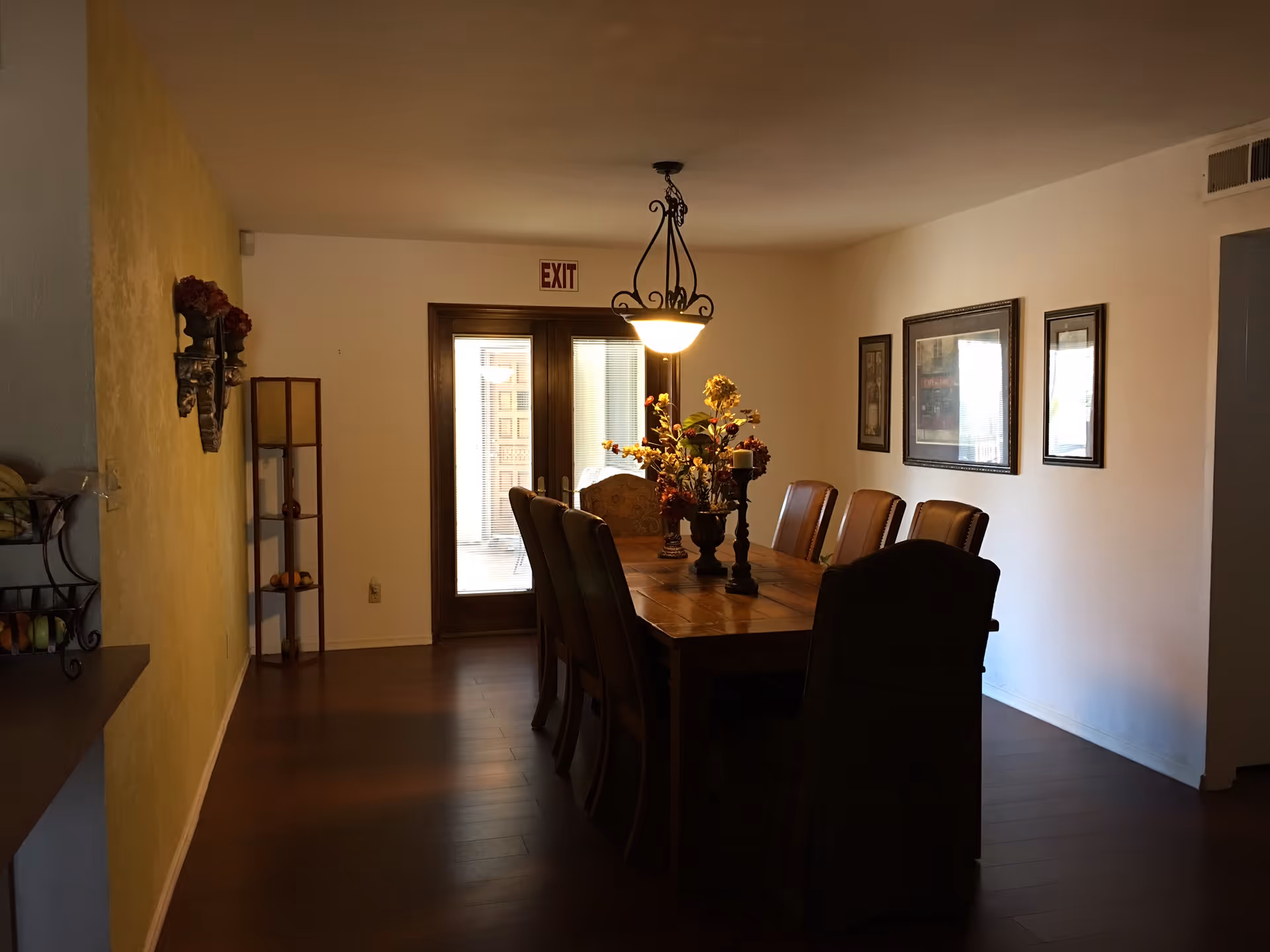 A dining room with a long wooden table, chairs, and a floral centerpiece.