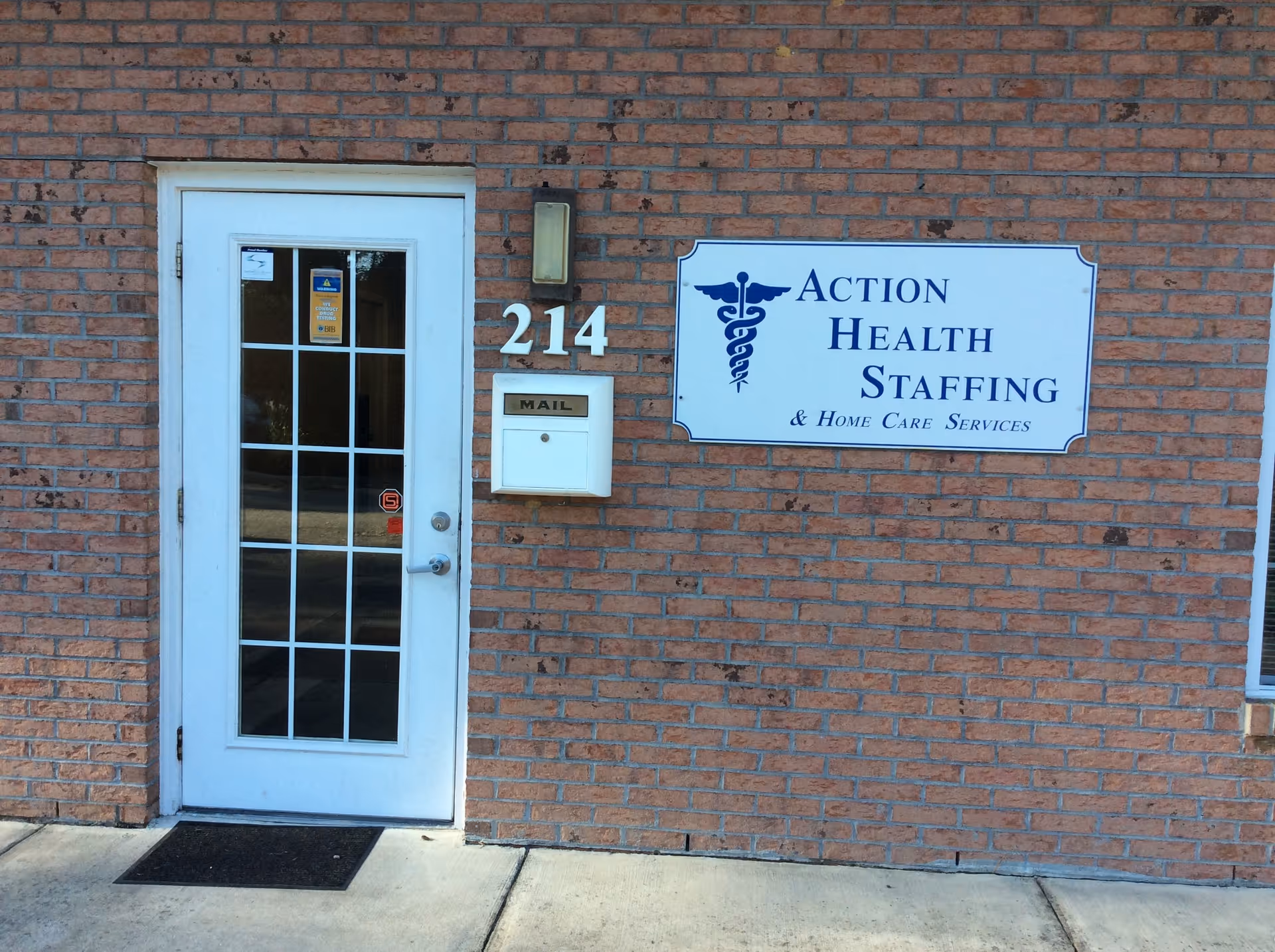 Brick building entrance with a white door and blue Action Health Staffing sign.