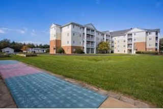 Exterior view of a multi-story senior living building with a green lawn and colorful walkway.