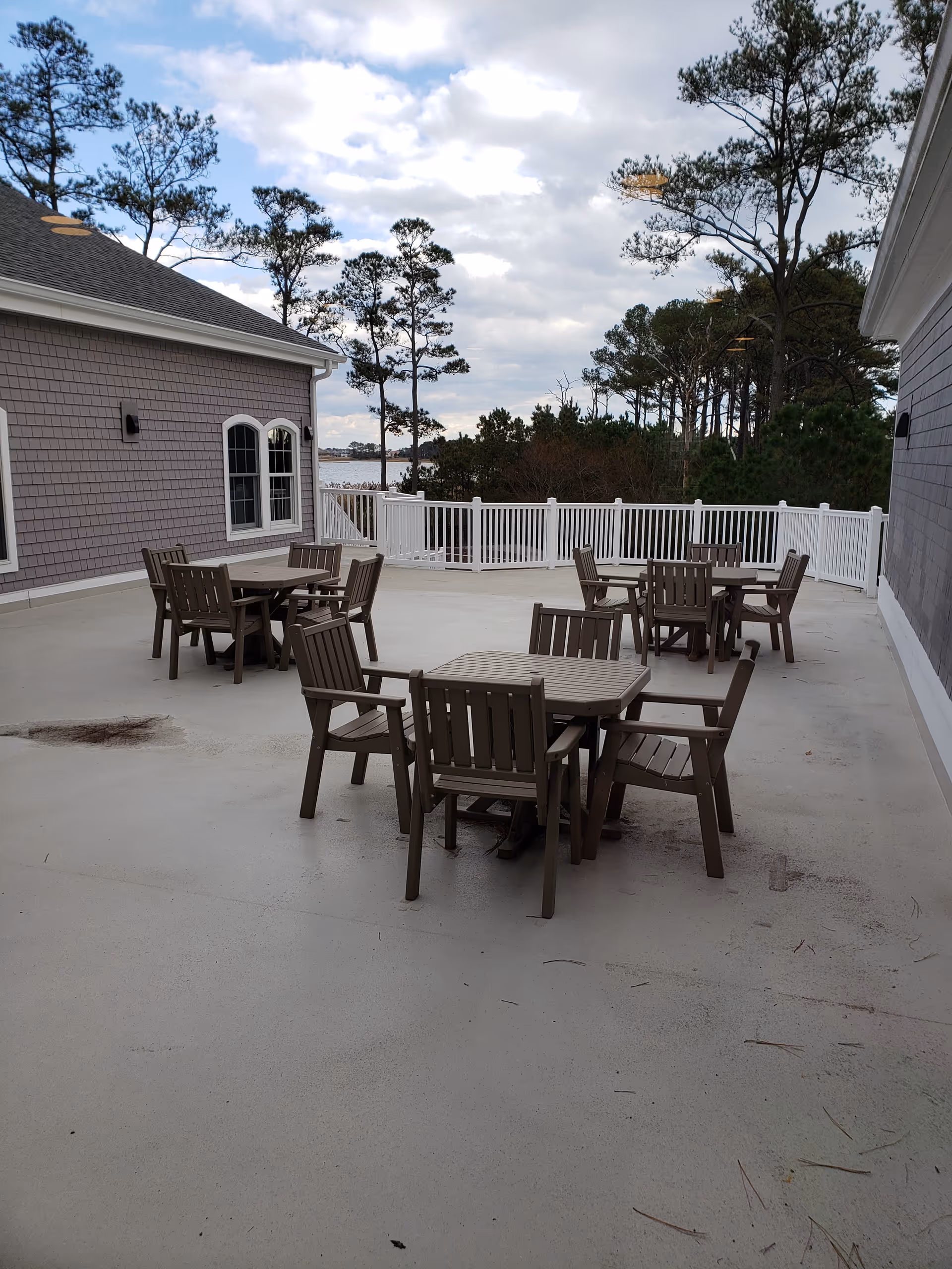 Outdoor terrace with wooden tables and chairs overlooking trees and distant water.