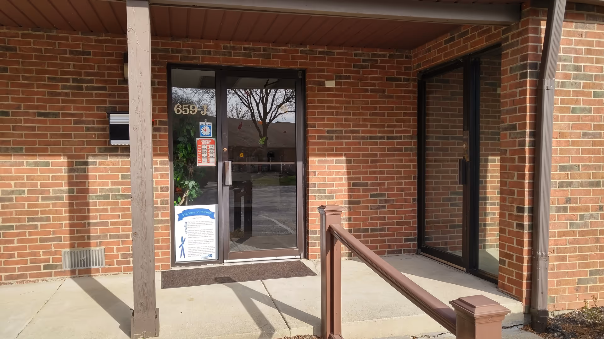 Brick facade with glass doors, concrete entry, and reflections at the building entrance.
