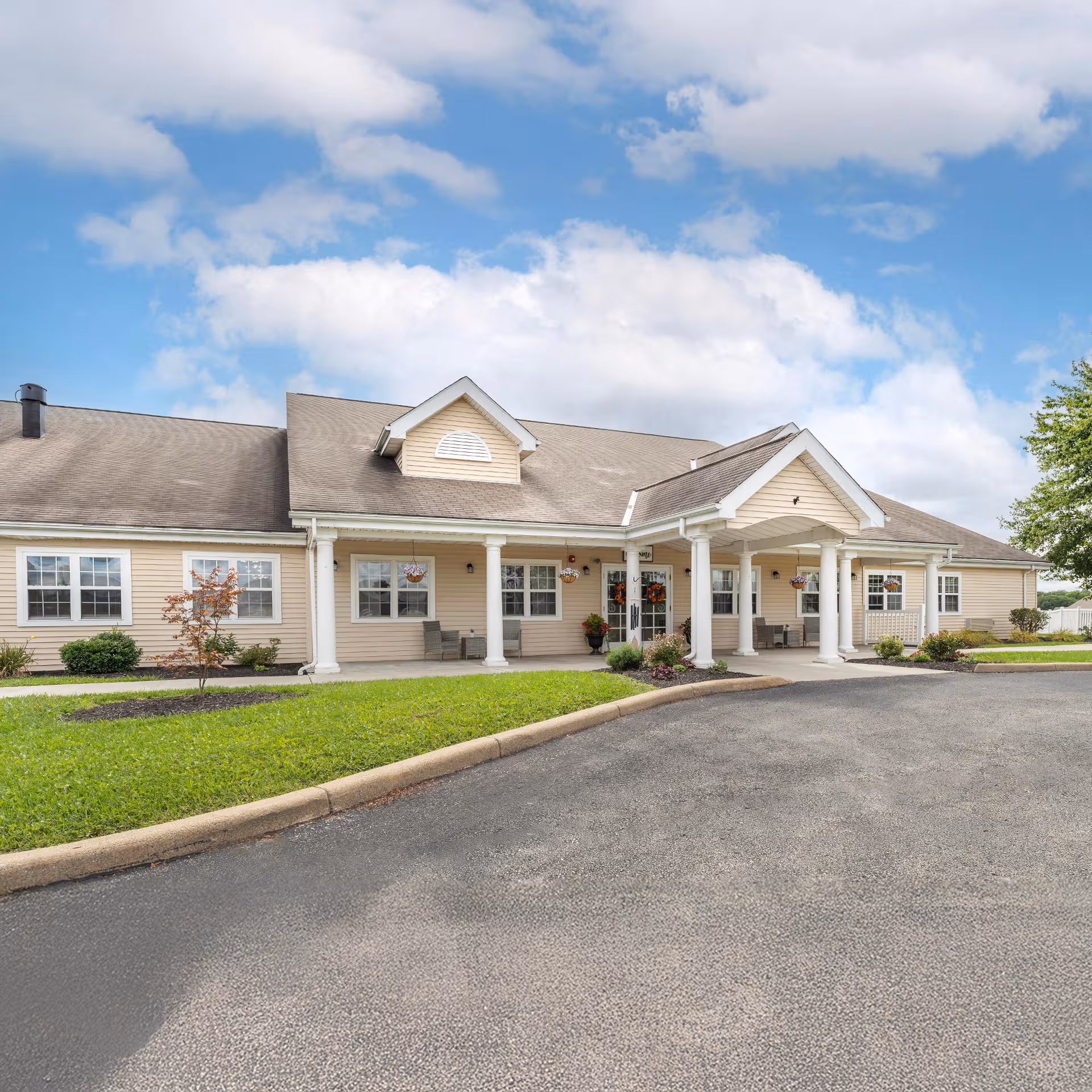 Single-story senior living facility with beige siding, white columns, and a curved driveway.