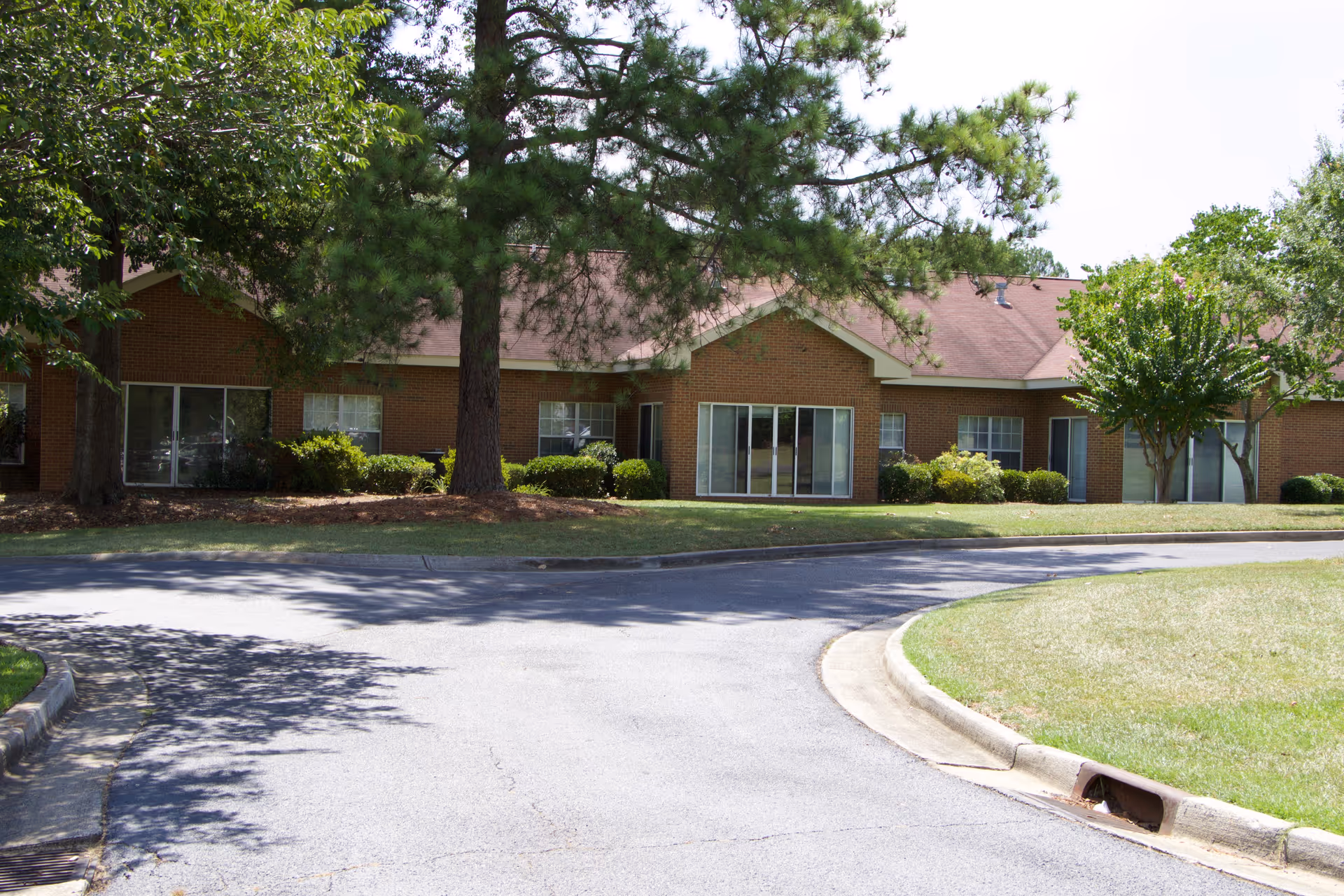 Brick single-story senior living facility with large windows, trees, and a curved driveway.