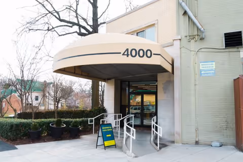 Entrance of a building with curved beige canopy, glass doors, and ramps.