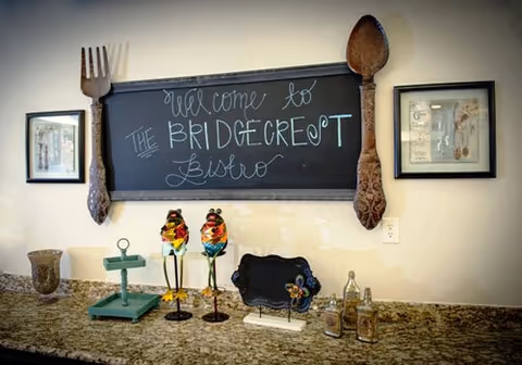 Granite counter with chalkboard sign, two colorful bird statues, and framed pictures in an interior.