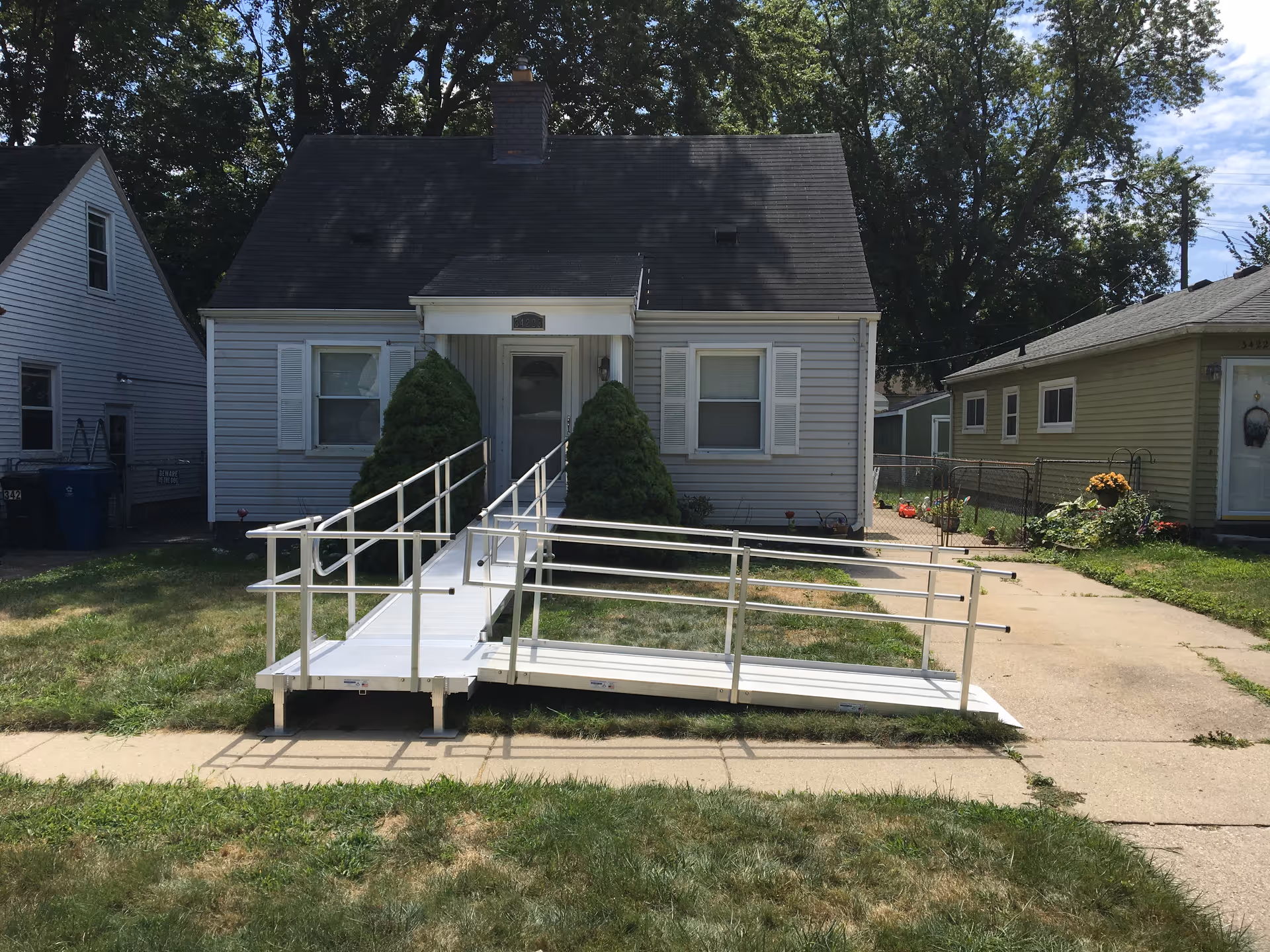 Front view of a small house with a white wheelchair ramp leading to the entrance