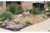 Exterior of a retirement community with landscaped garden and a small American flag by the walkway.