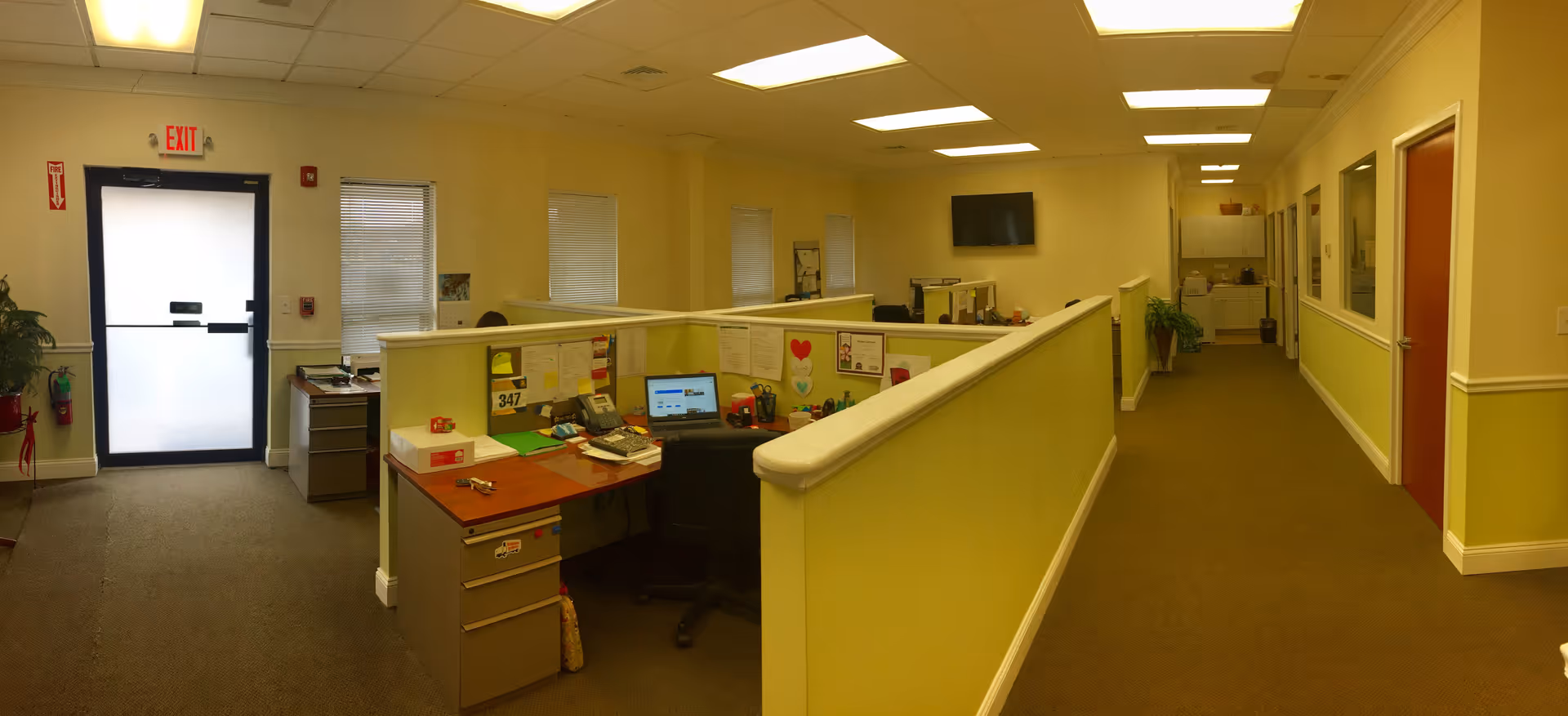 Interior office-like reception area with cubicles and a long hallway in a senior care facility.