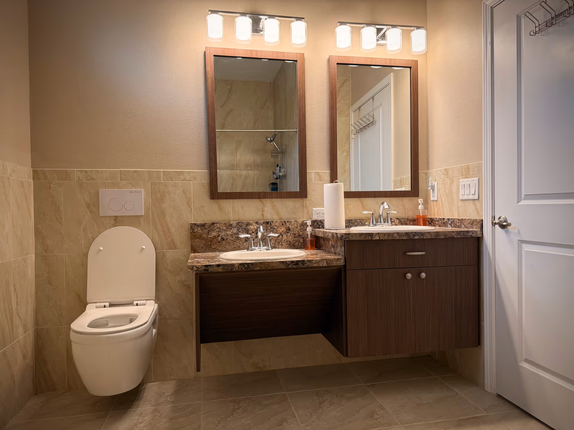 Modern bathroom with dual sinks, two mirrors, a wall-mounted toilet, and beige-tiled walls.