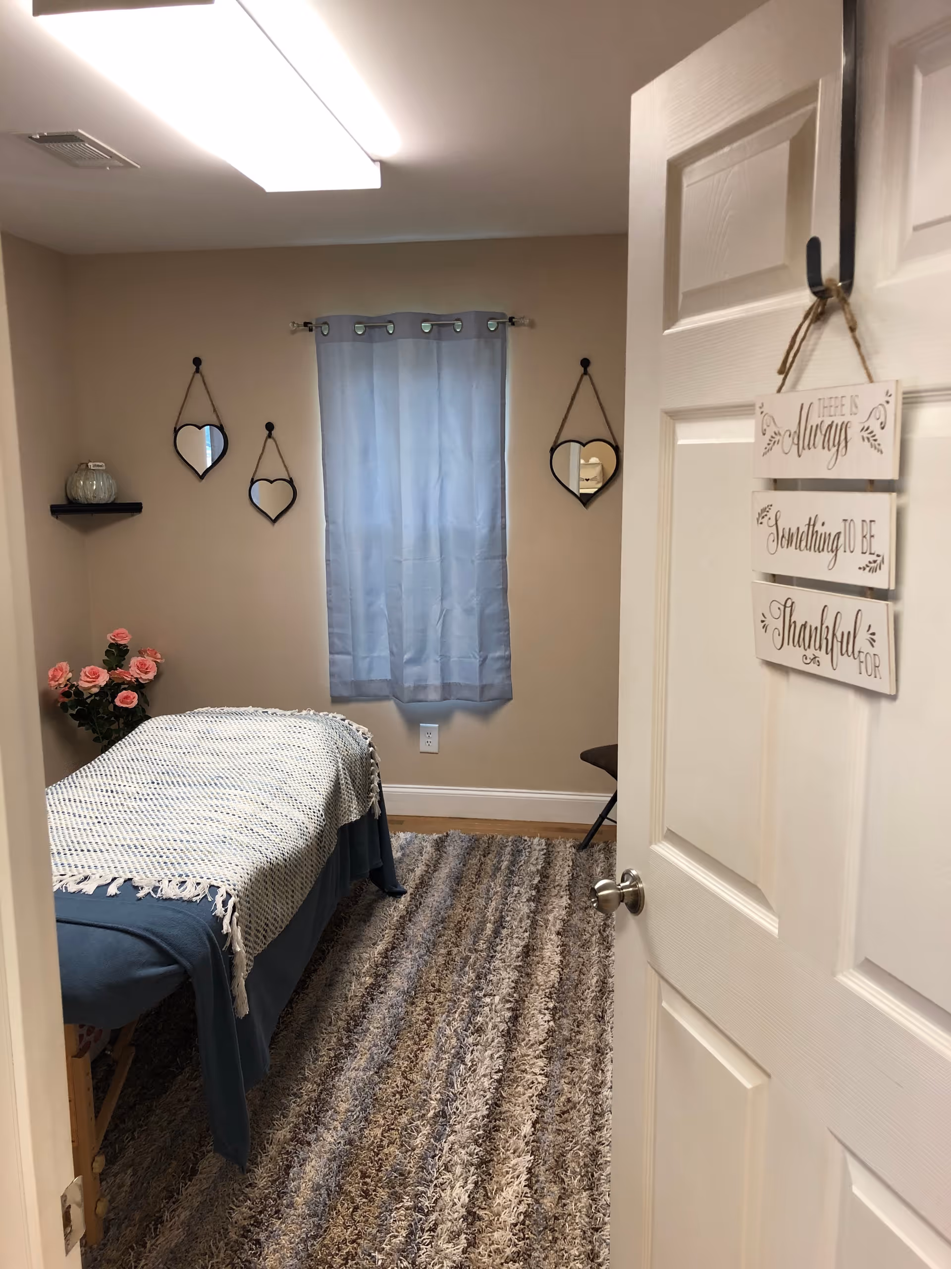 A small cozy bedroom with a bed, blue curtain, heart mirrors, and floral bouquet.