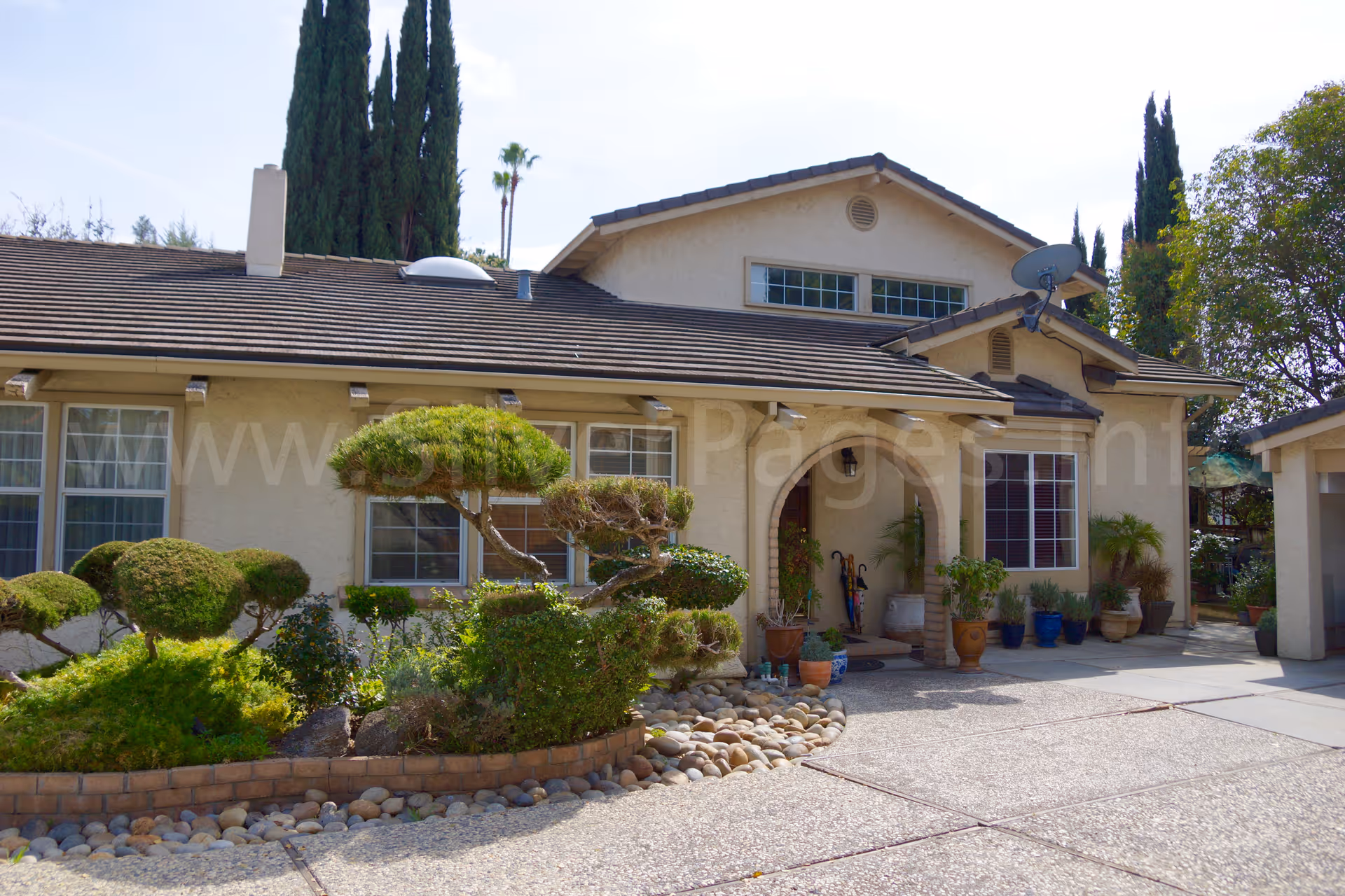 Front exterior view of a single-story senior home with arched entry and potted plants.