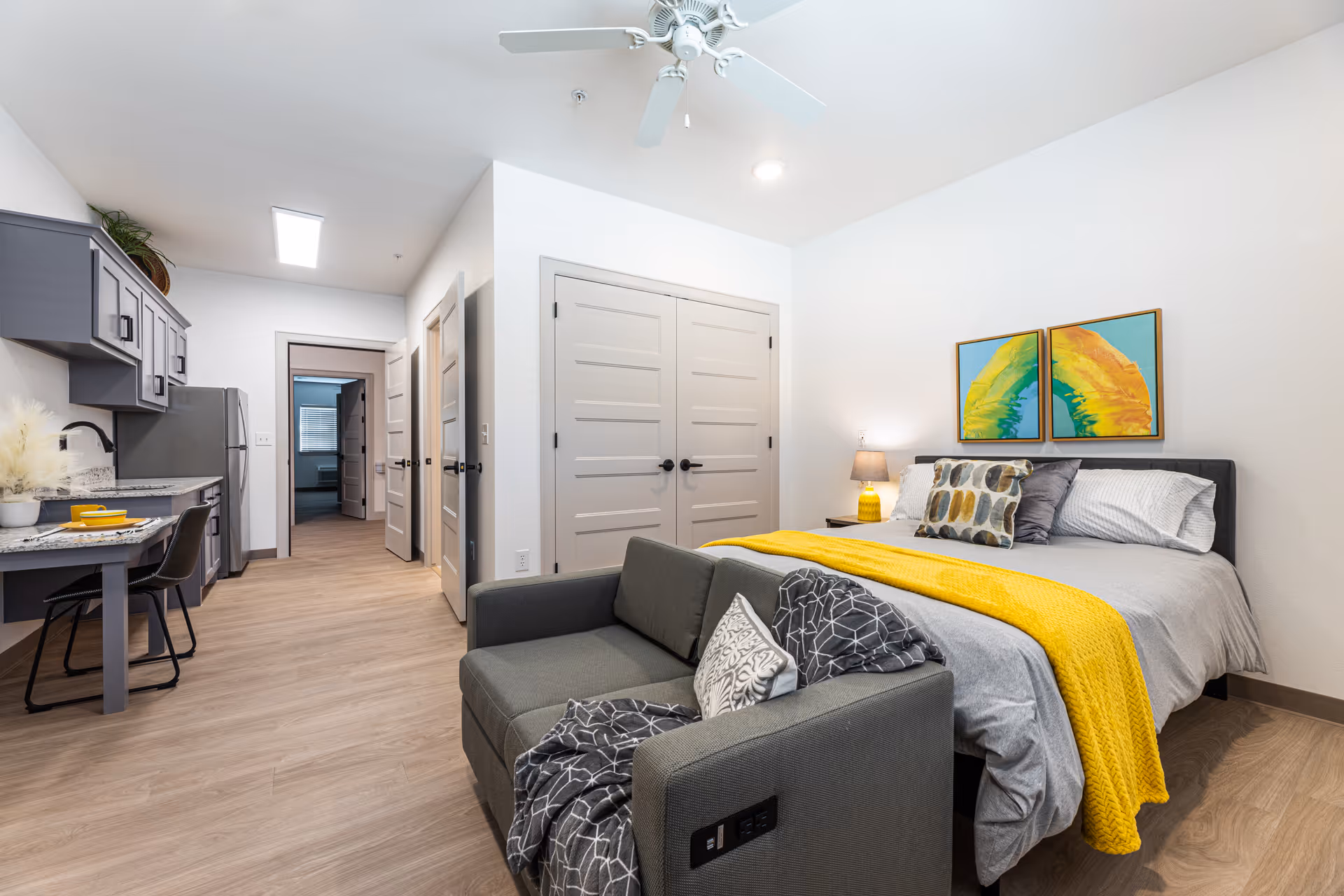Modern furnished senior living studio with bed, sofa, kitchenette, and dining area.