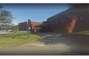 Brick nursing home building with driveway and manicured lawn under a clear blue sky.