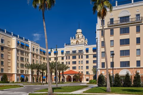 Large Mediterranean-style multi-story senior living building with palm trees and a circular driveway under a clear blue sky.