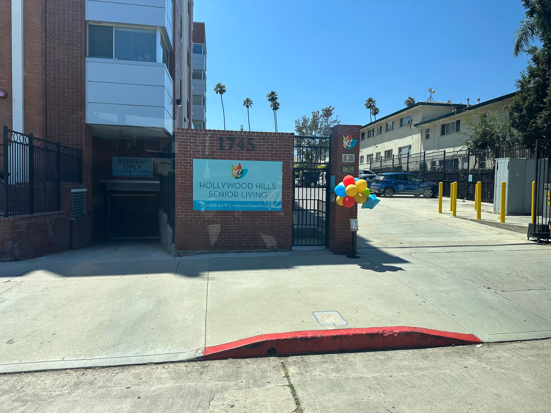Exterior view of Hollywood Hills Senior Living entrance with sign, balloons, and gated driveway.