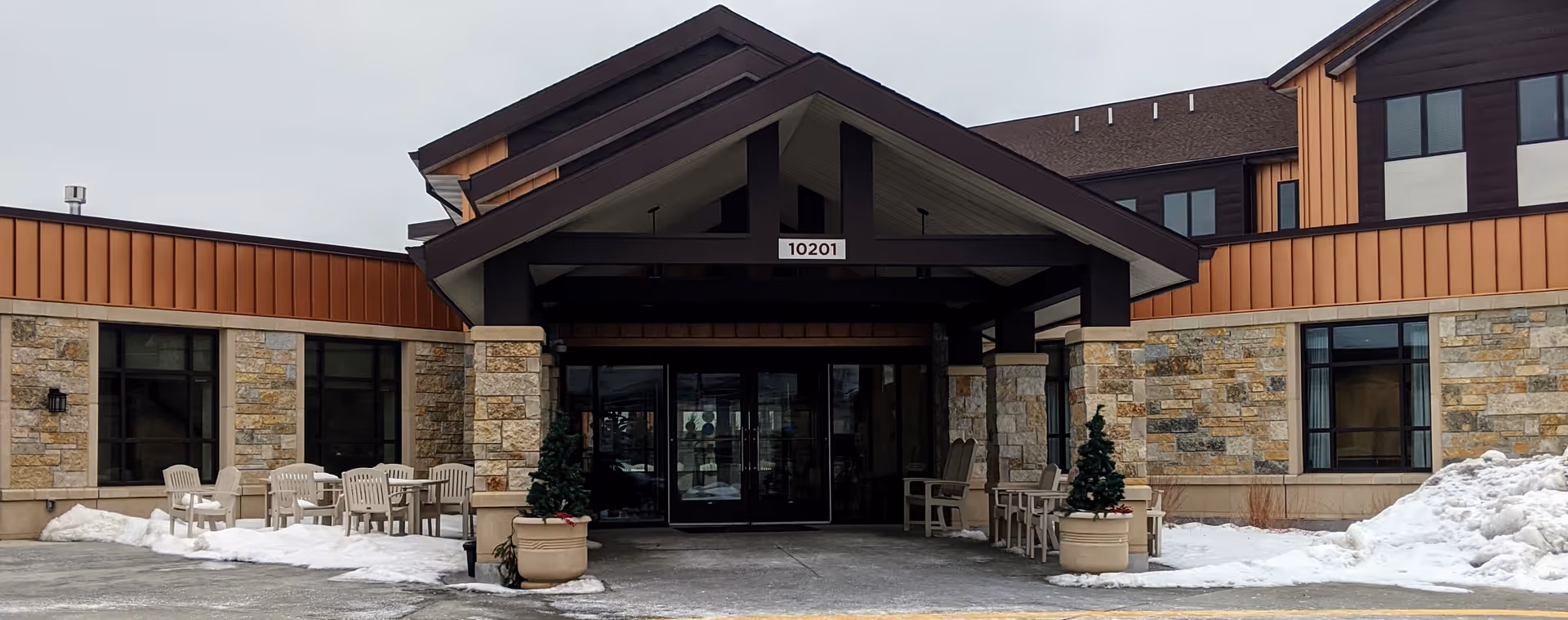Front entrance of a senior living facility with snow, stone walls, and outdoor seating.