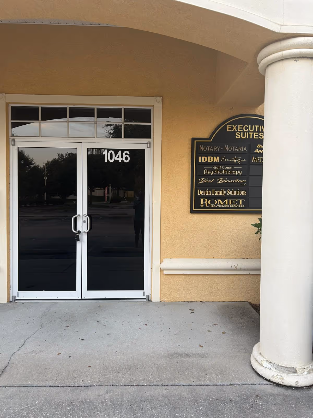 Beige exterior building entrance with double glass doors numbered 1046 and a black business sign.