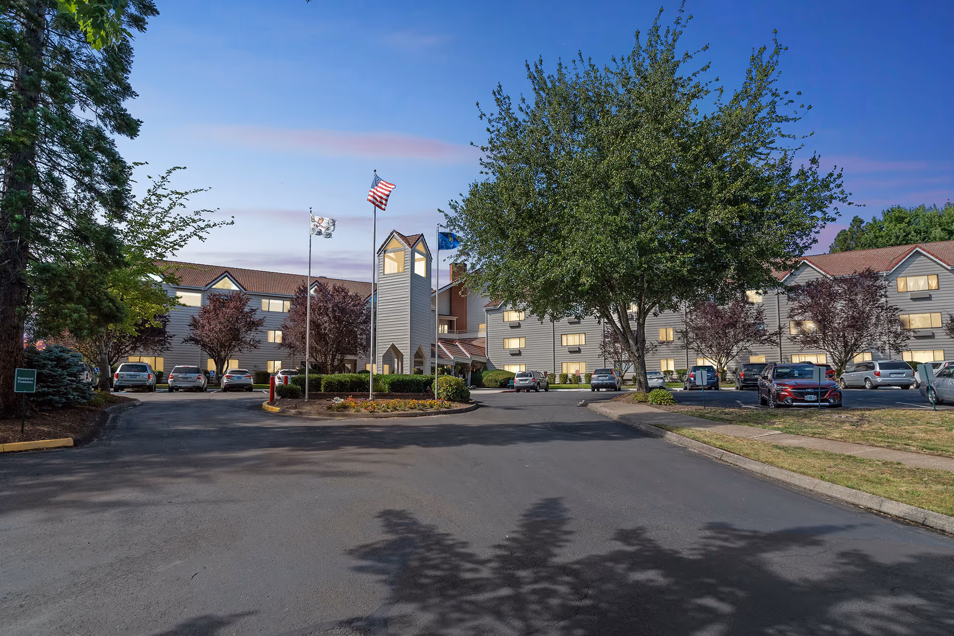 Exterior view of Solista Milwaukie senior living campus with driveway, flags, and trees.