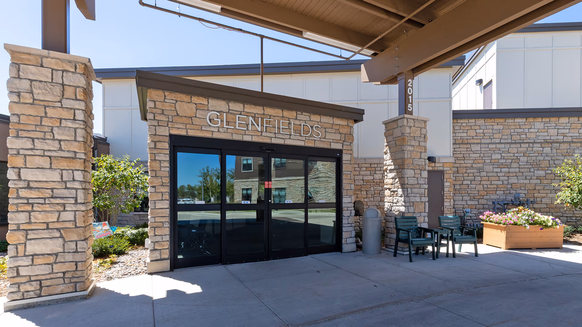 Front entrance of GlenFields with stone pillars, glass doors, chairs, and planters