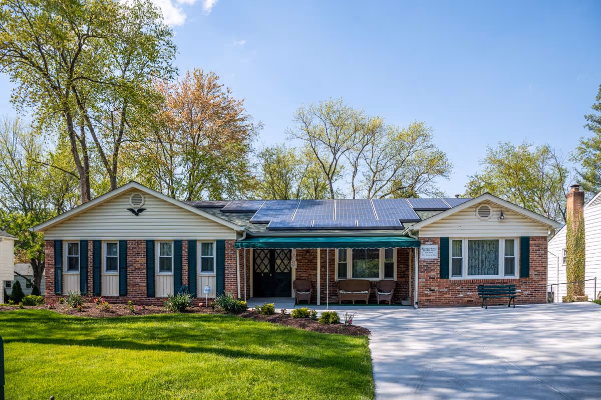 A one-story brick senior living facility with solar panels and a shaded front entrance with seating.