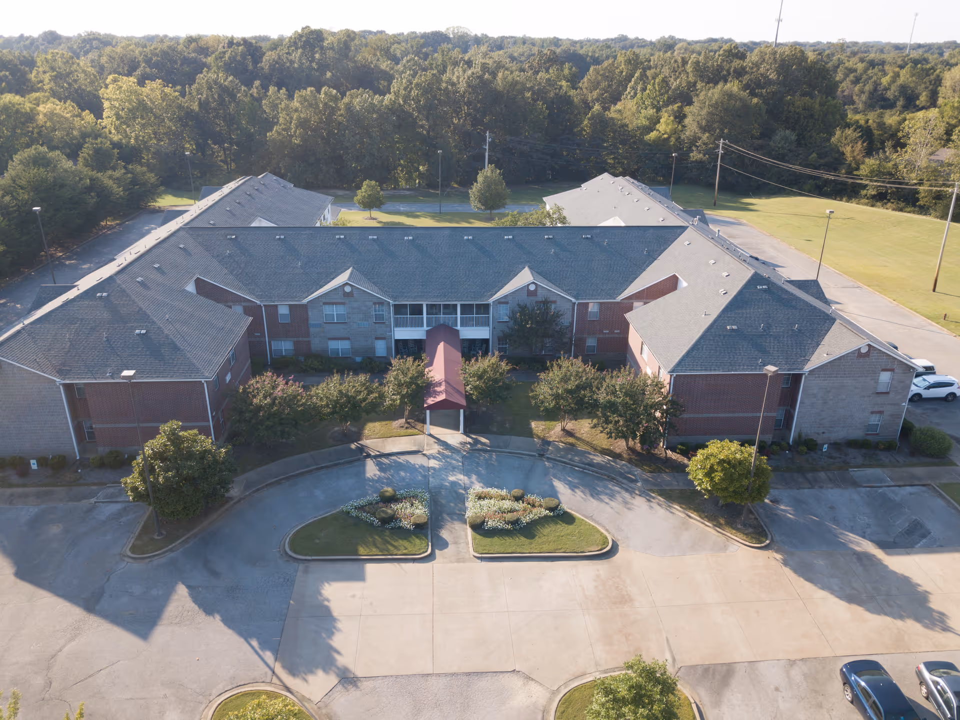 Aerial front view of a two-story senior living building with a covered entrance, circular driveway, and surrounding trees.