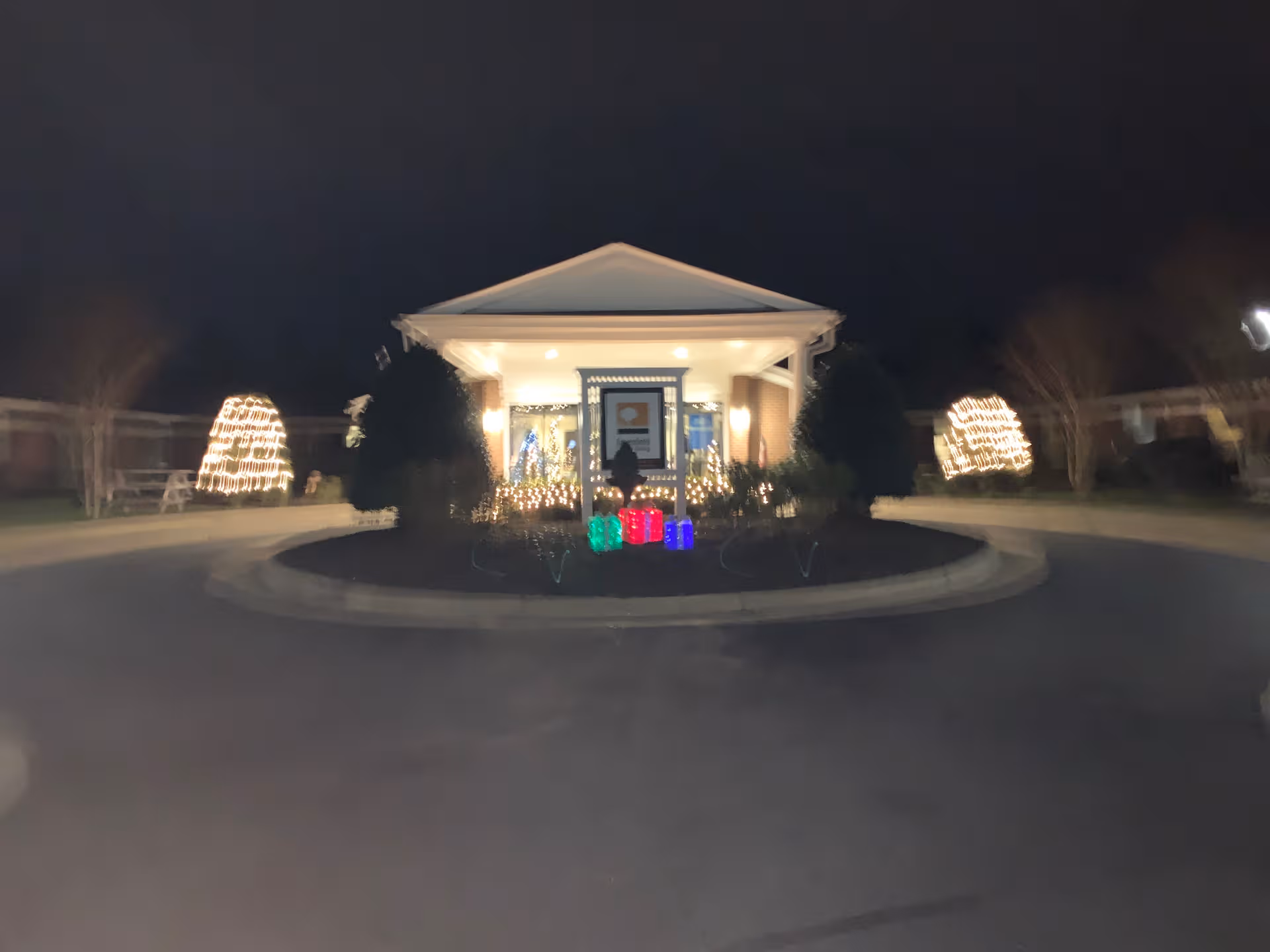 Night view of Mic and Assisted Living entrance with illuminated holiday decorations and a circular driveway.