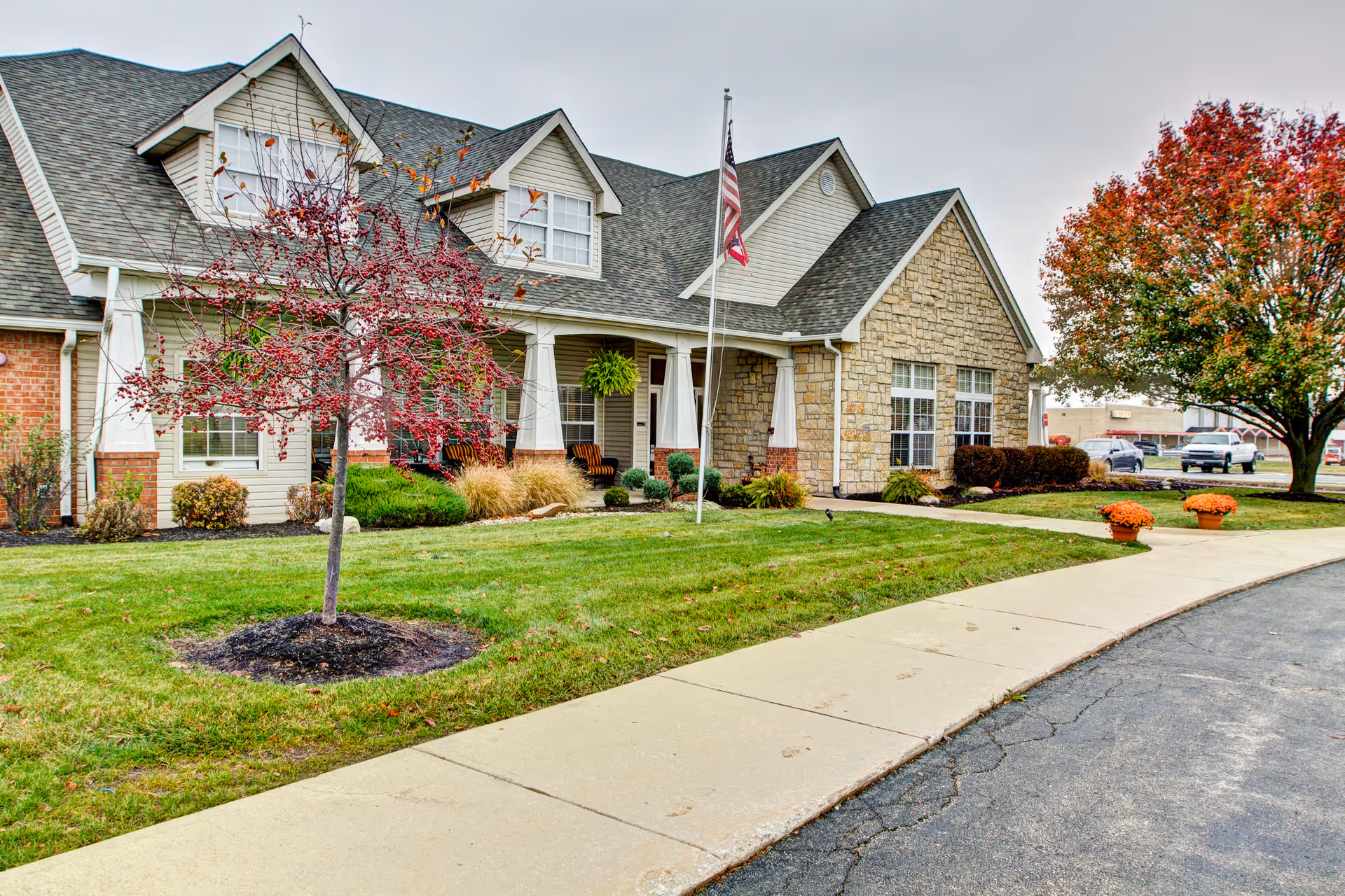 Brookdale Piqua facility exterior with lawn, trees, and a flagpole.