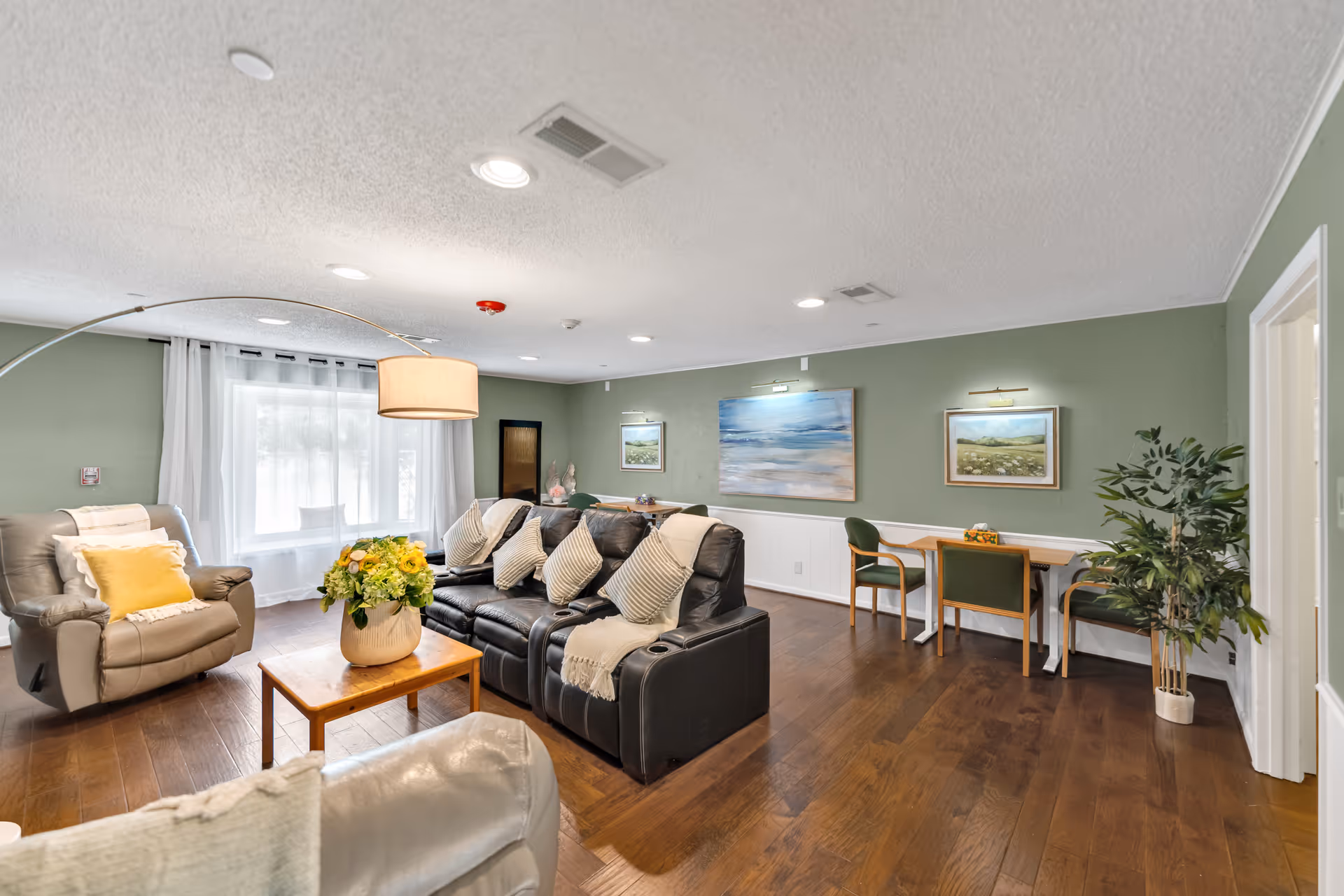 Spacious living room with green walls, leather sofas, a coffee table, and wall art.