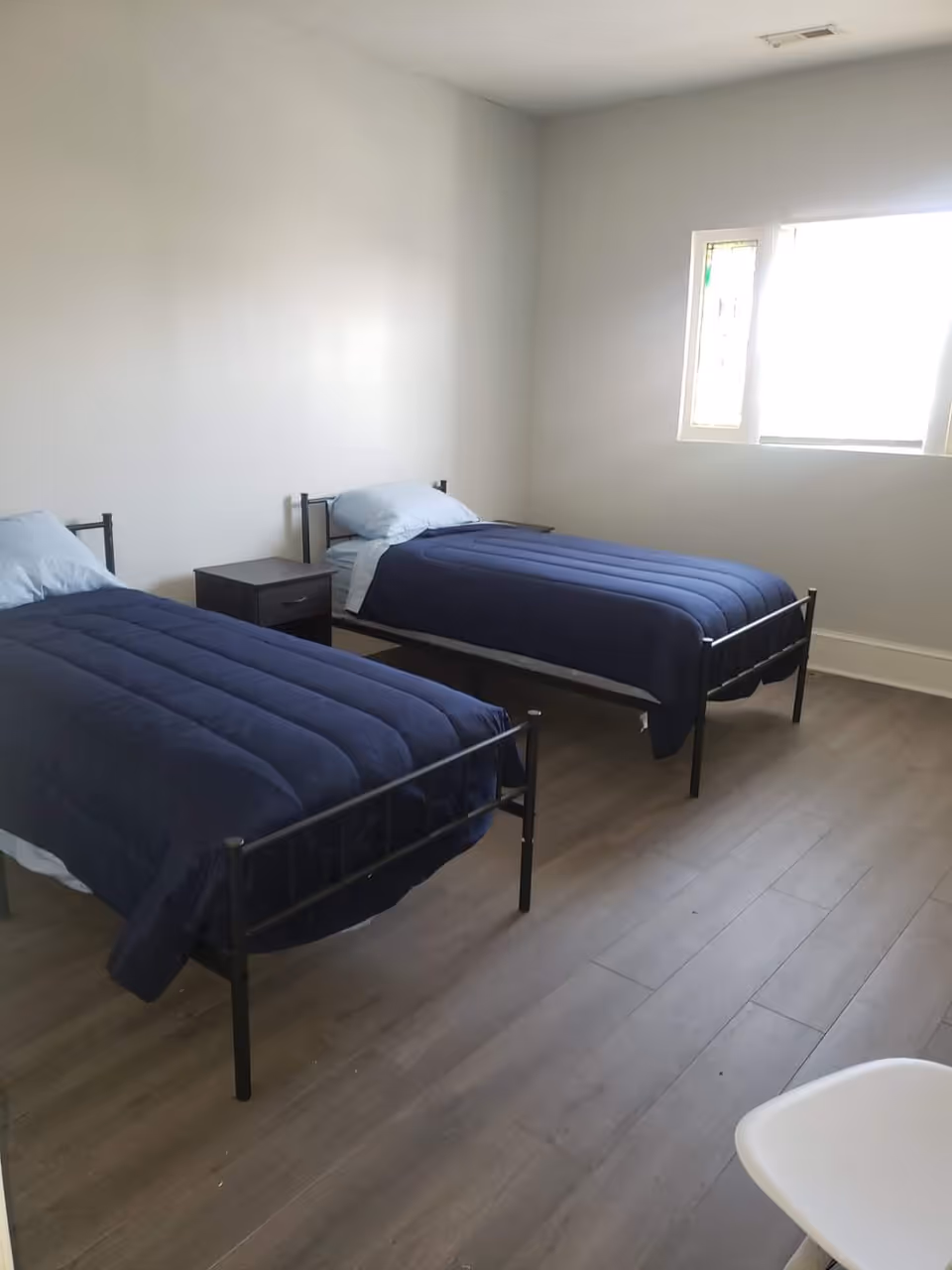 Two twin beds with navy duvets in a sparsely furnished bedroom.