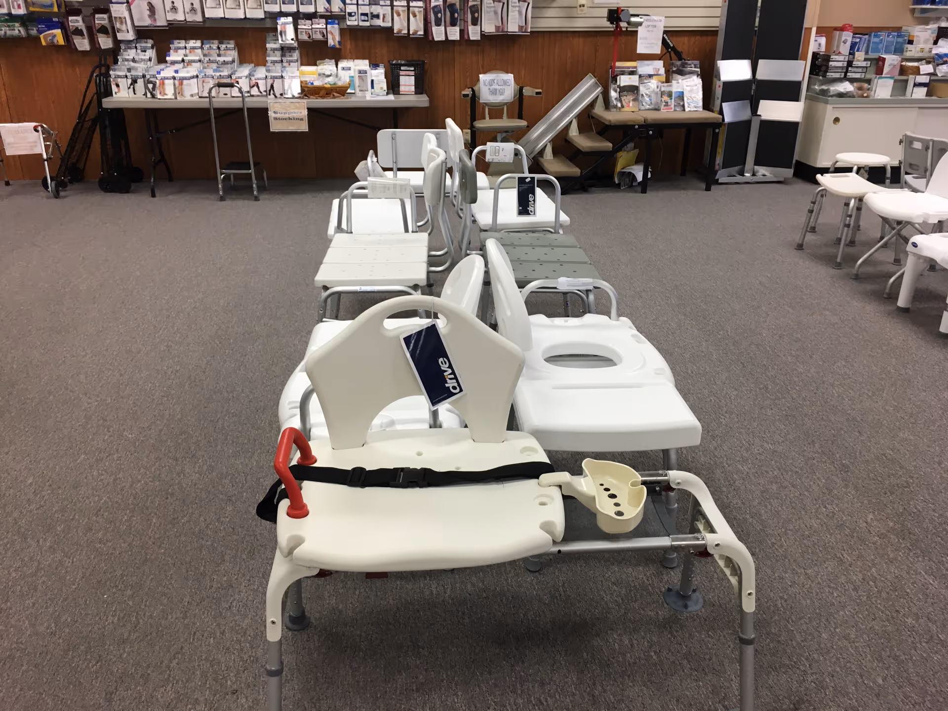 Row of patient transfer chairs and commodes in a medical equipment showroom.
