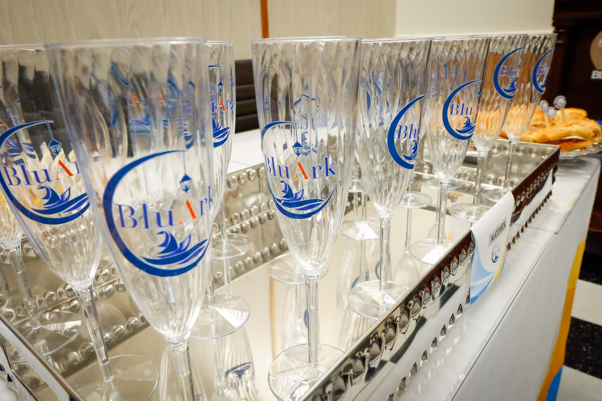 Close-up of crystal champagne flutes with BluArk logos on a catering counter