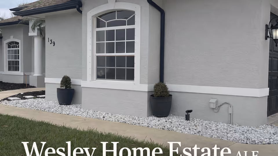 Front exterior of a gray assisted living facility with arched window and planters.