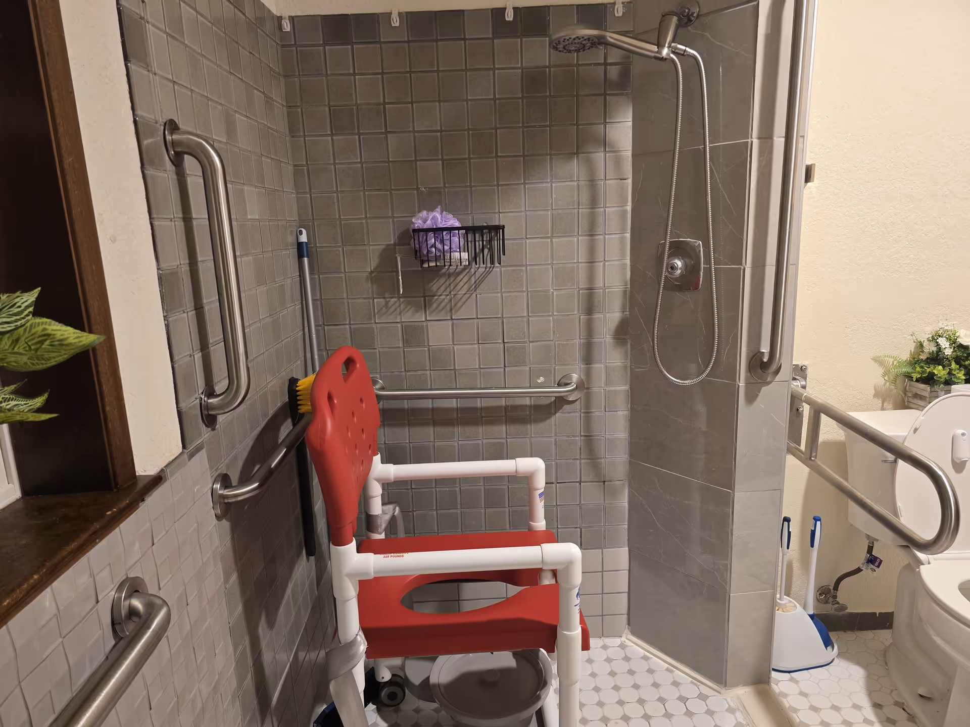 Accessible bathroom with a red shower chair, grab bars, and a handheld shower.